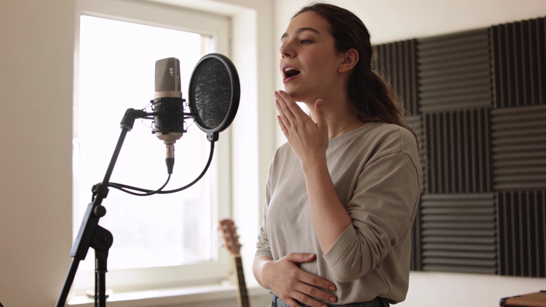 young woman practicing vocal warm-ups in a home studio with one hand on her stomach and the other near her throat