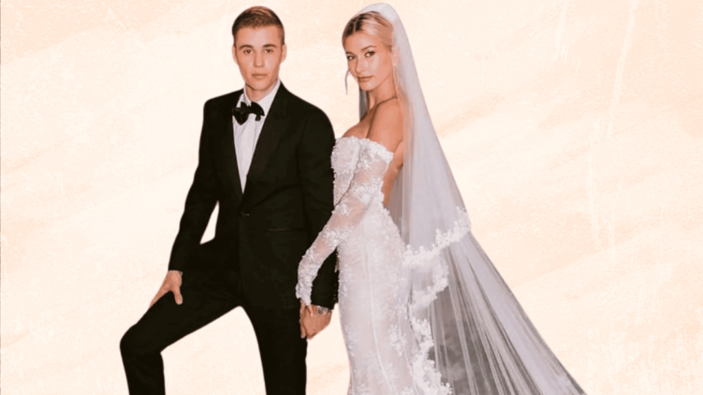 Bride and groom in wedding attire with long veil against a soft peach background