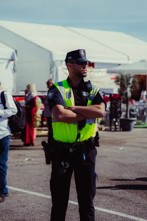 Police officer in high-visibility vest standing outdoors at public event with tents in background
