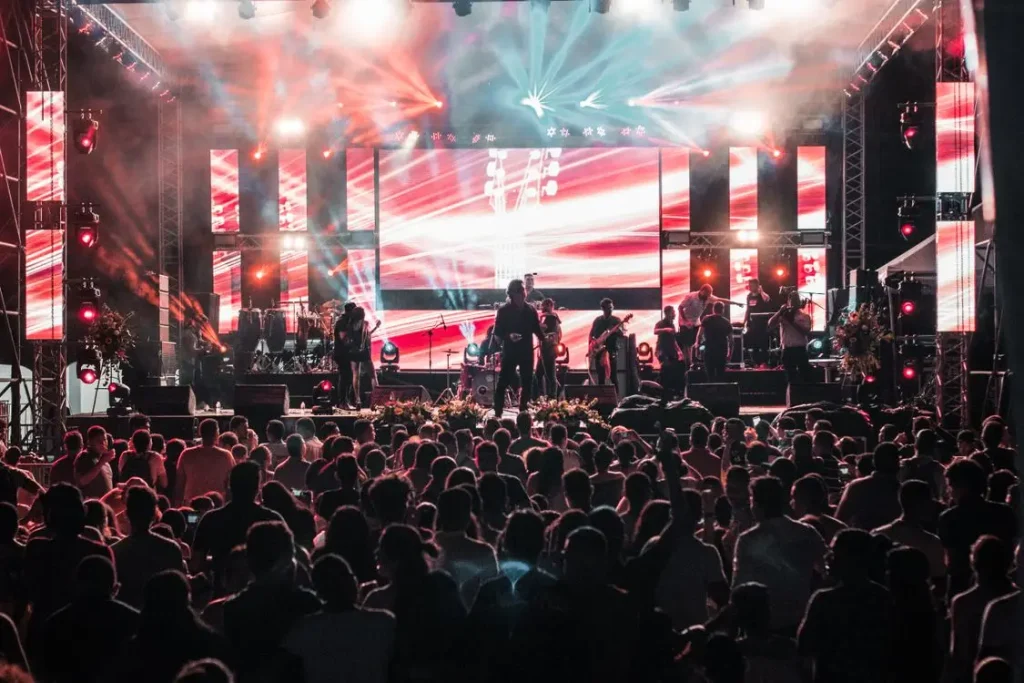 Concert stage with band performing under vibrant red and blue lights in front of large crowd