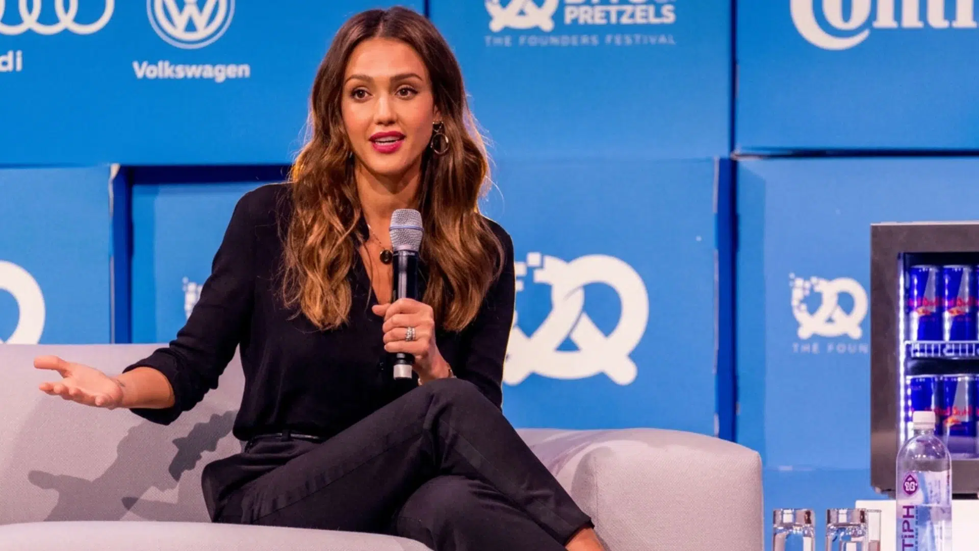 Jessica Alba speaking into a microphone while seated onstage at a business event.