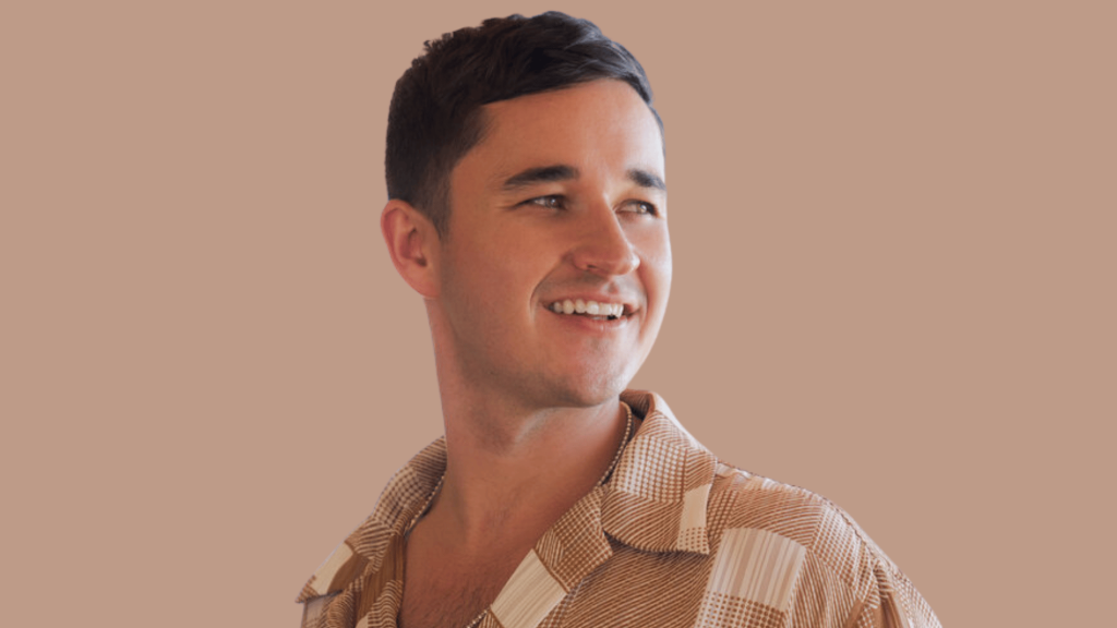 Smiling man in patterned shirt looking aside against a plain beige backdrop