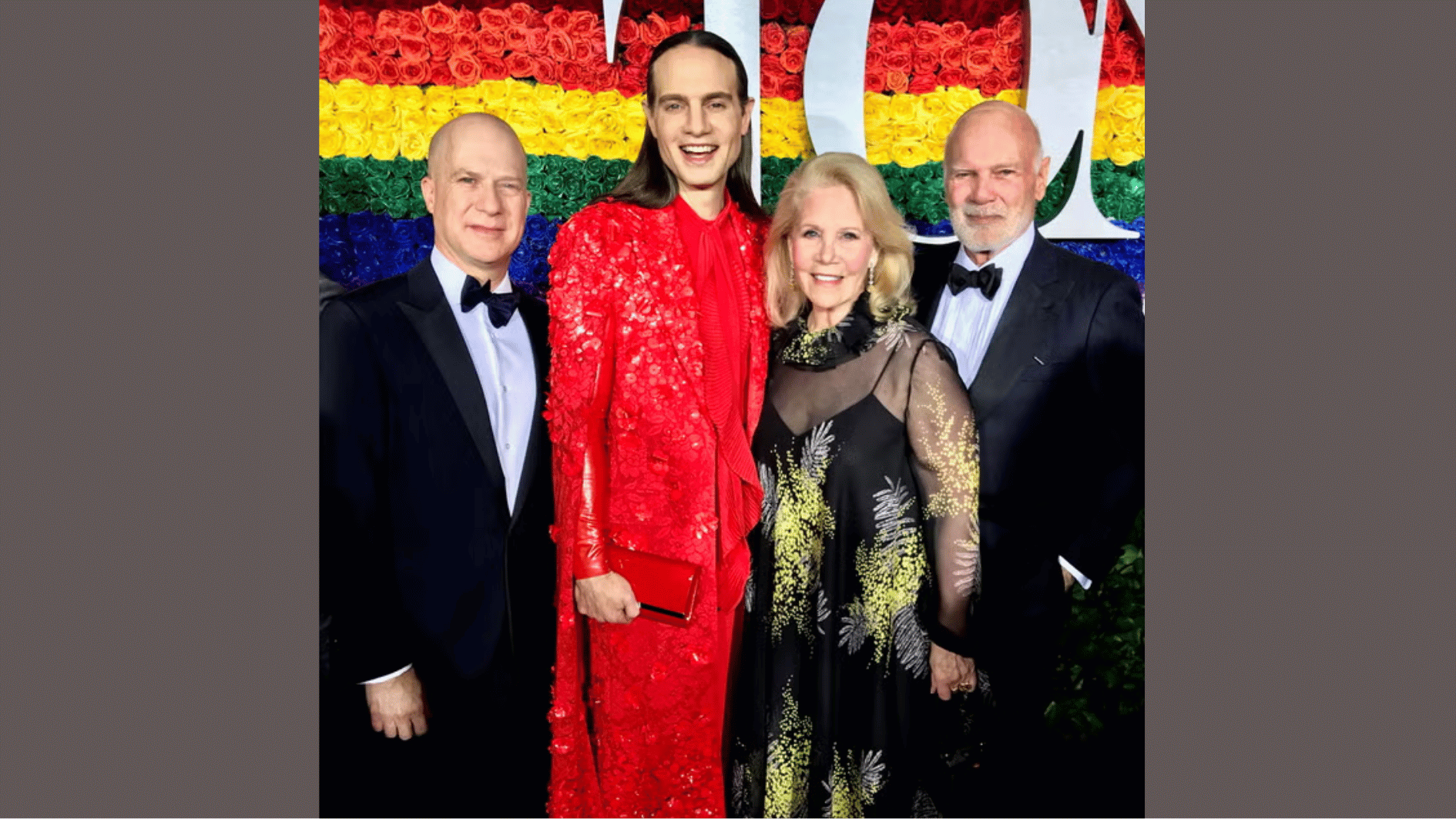 jordan roth in a bold red look, standing with family members in front of a rainbow backdrop at an lgbtq+ pride event.