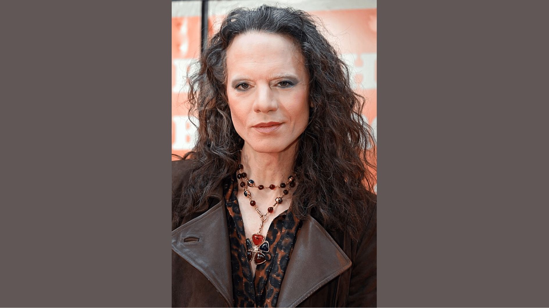 jordan roth with long, curly dark hair wearing a brown leather jacket and layered necklaces.
