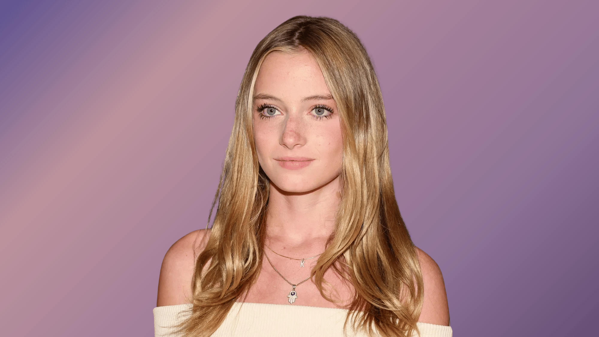 Portrait of Kai Schreiber with long blonde hair, wearing an off-shoulder top against a purple backdrop.