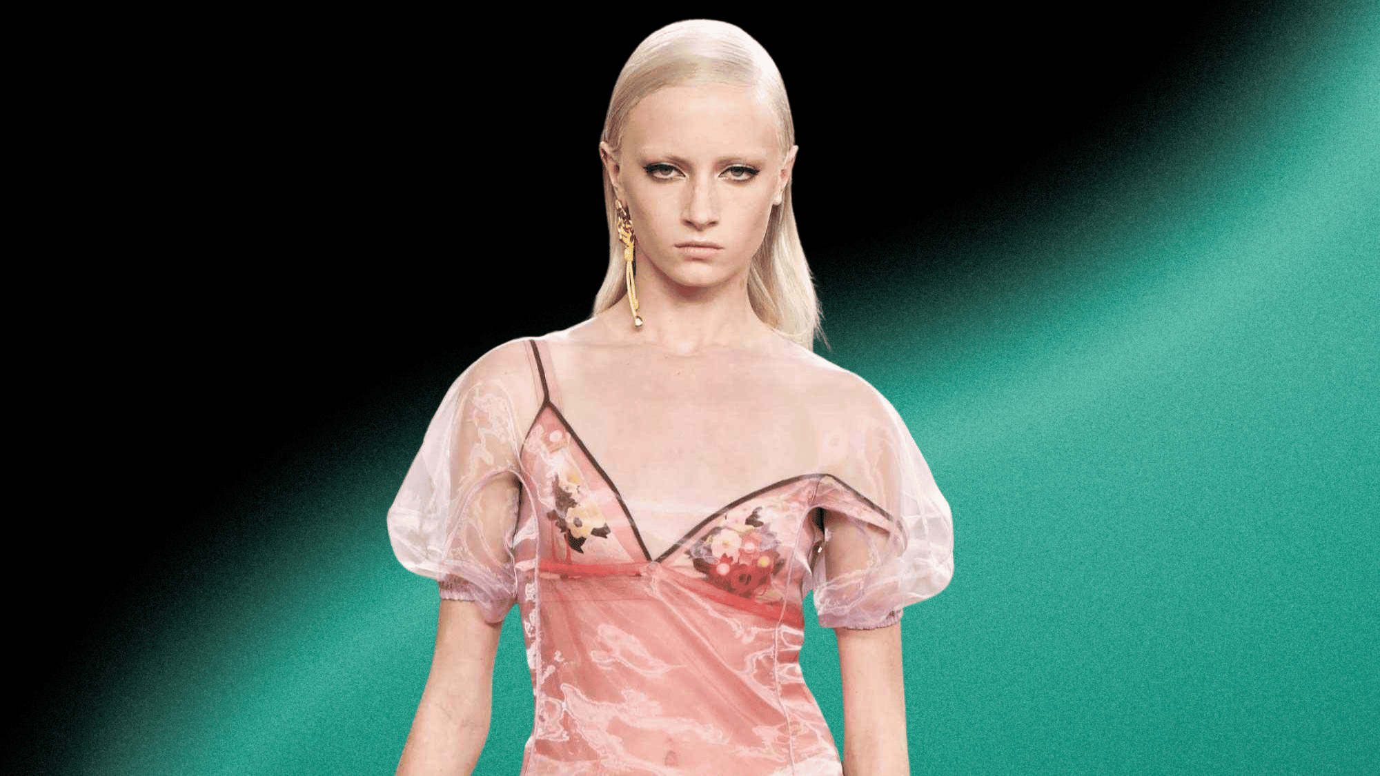 Kai Schreiber walking the runway in a sheer pink dress during a fashion show with dramatic lighting.