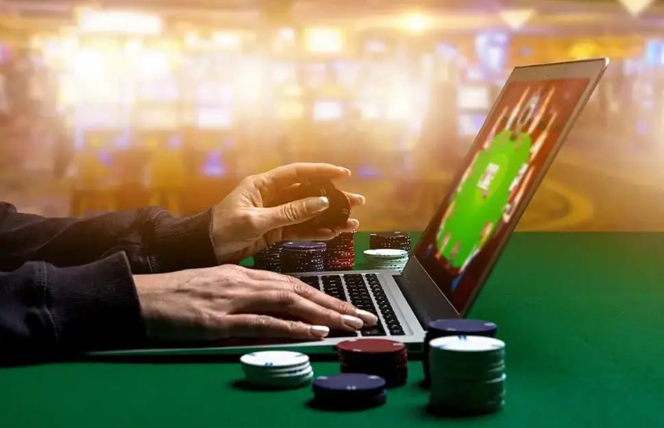 Hands playing online poker on laptop with poker chips on green table