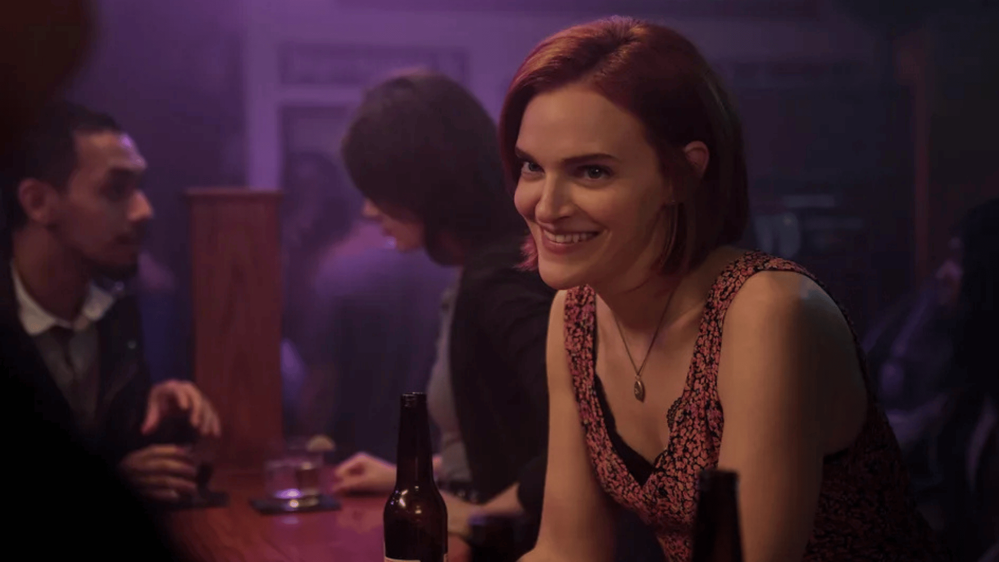 Woman smiling at a dimly lit bar with people in the background
