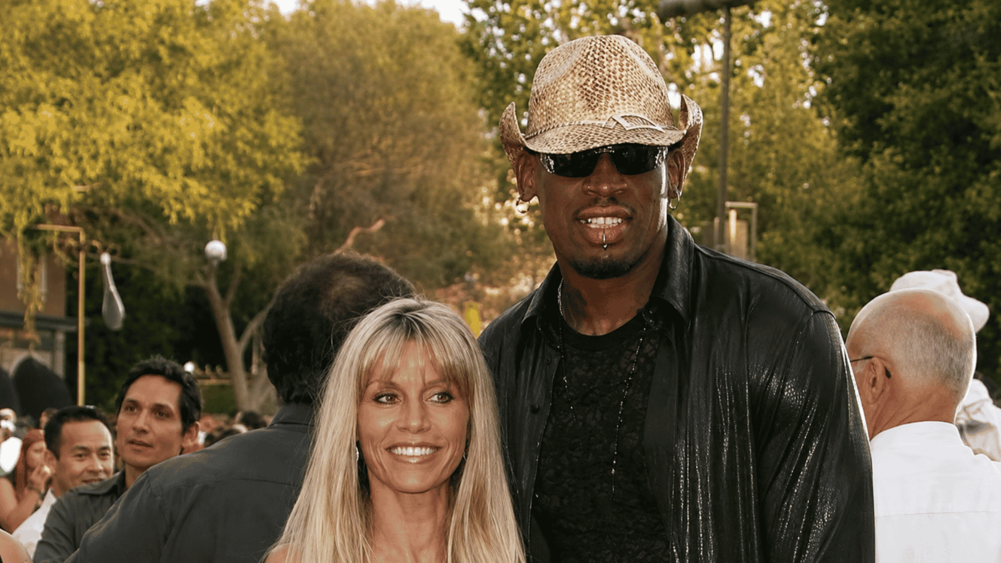 Tall man in a cowboy hat posing with a blonde woman at an outdoor event