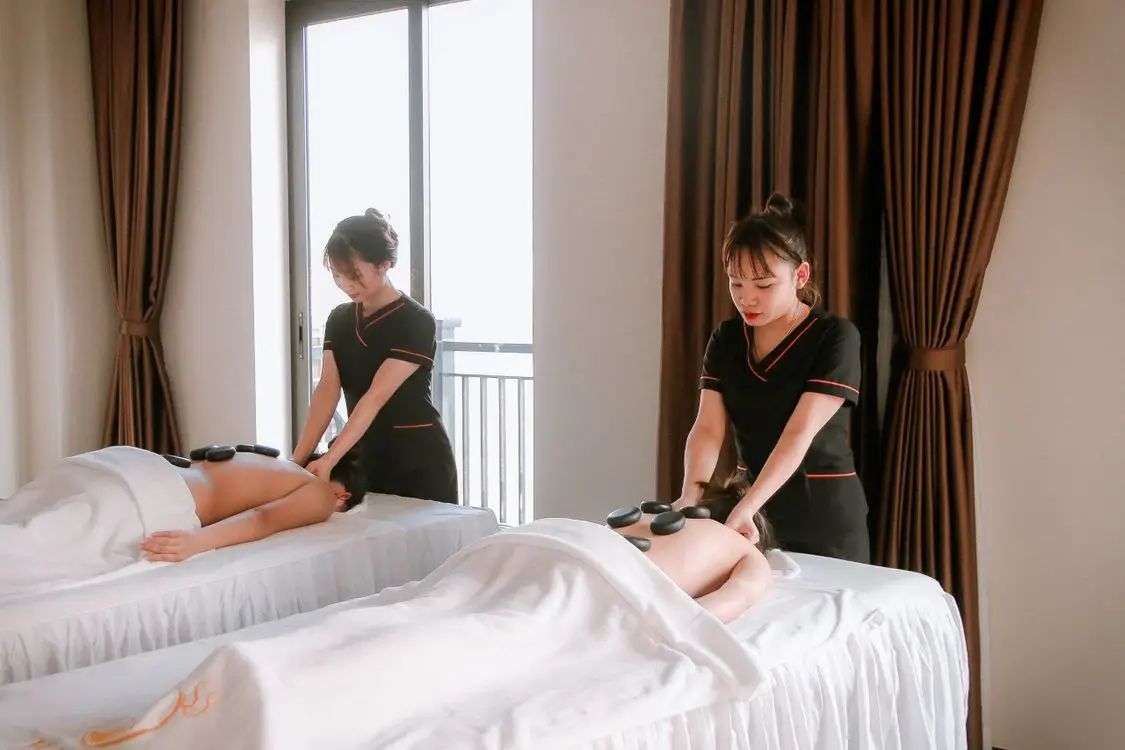 Massage therapist giving a hot stone treatment to a client on a white-covered table