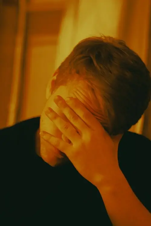 Man covering face with hand under warm indoor lighting