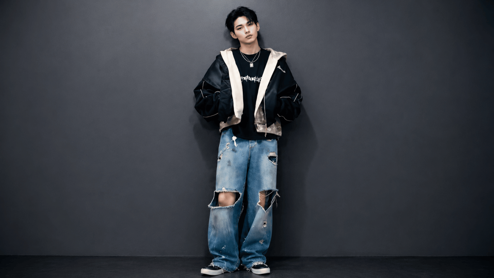 Ni-ki poses in layered streetwear and ripped jeans against a dark industrial studio wall.