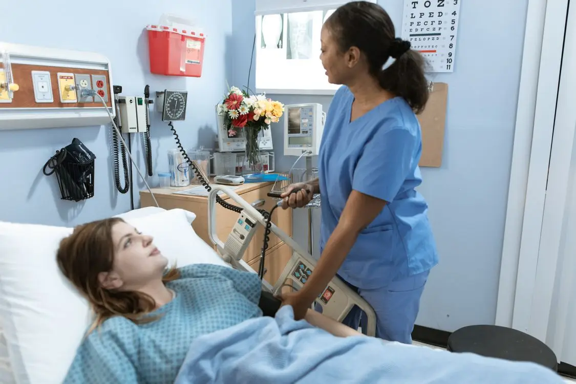 Nurse in blue scrubs attending to a patient in a hospital room with medical equipment
