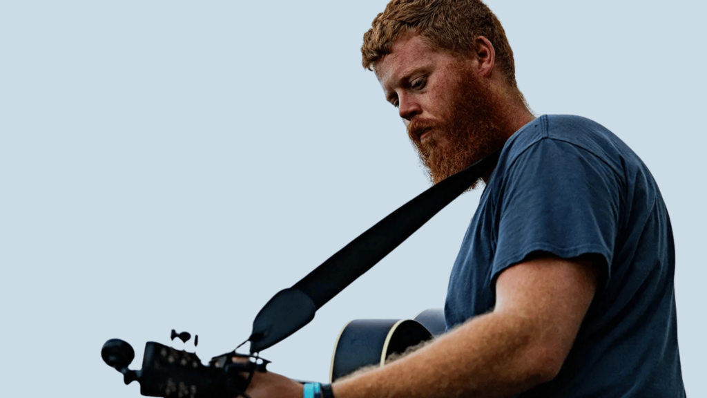 Bearded country singer holding a guitar against a clear sky background