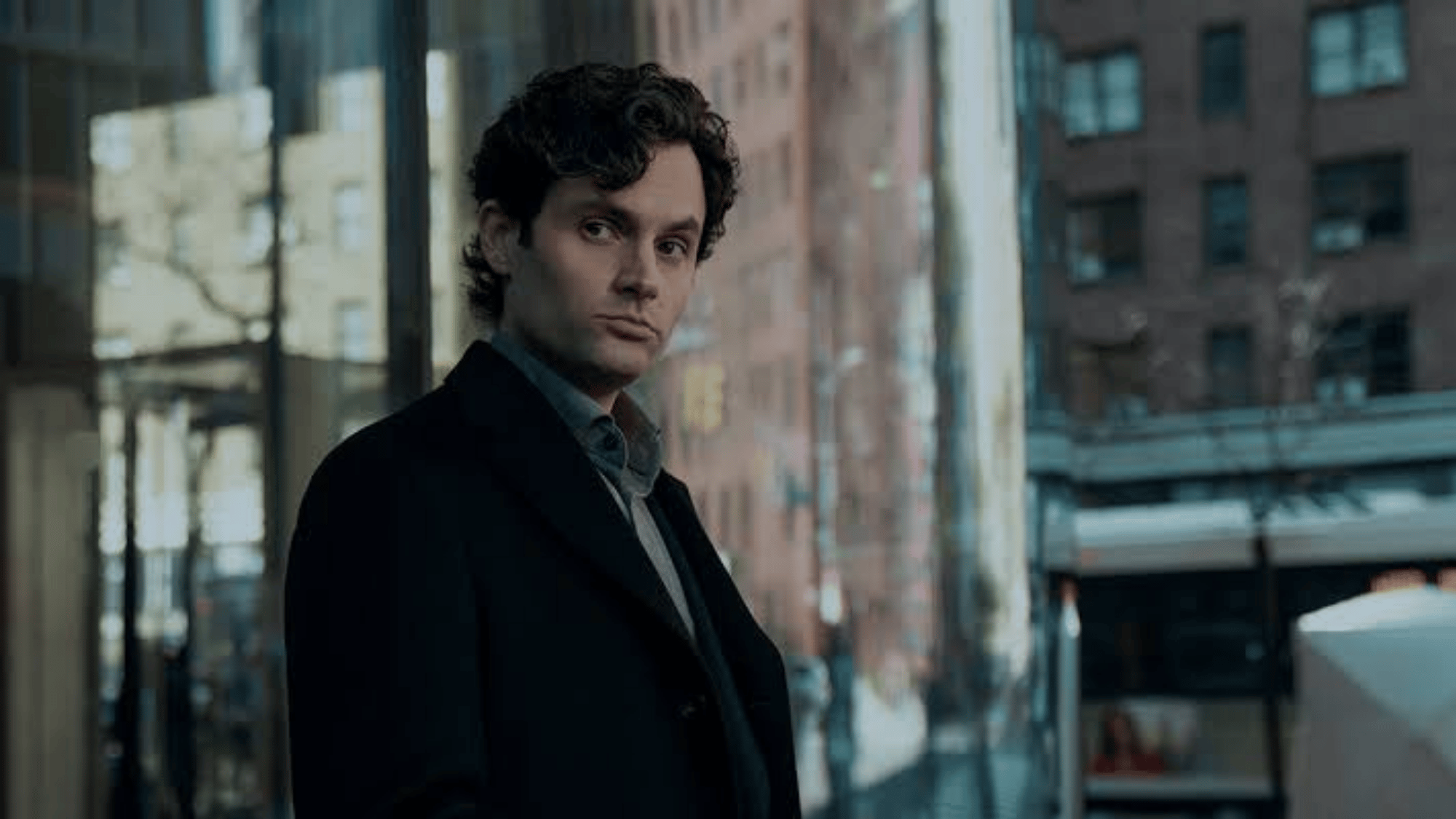 Man in dark coat standing near glass windows in a city building