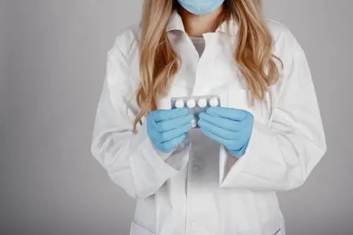 Female scientist in lab coat holding blister pack of pills with blue gloves