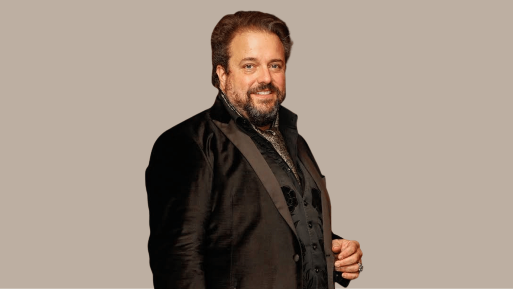 raul malo smiling in a black velvet tuxedo jacket against a neutral background