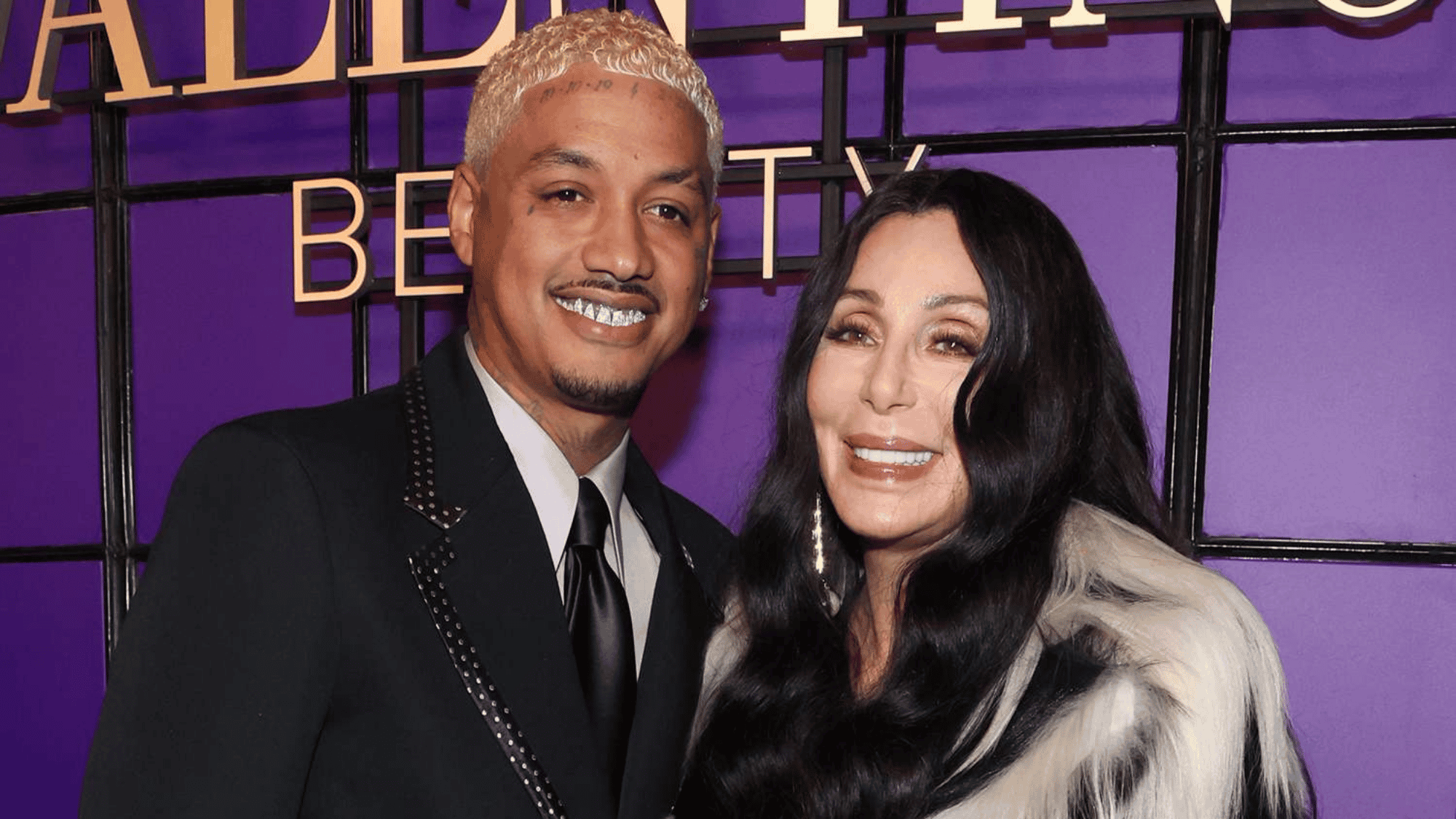Singer posing with her partner at a public event against a purple backdrop