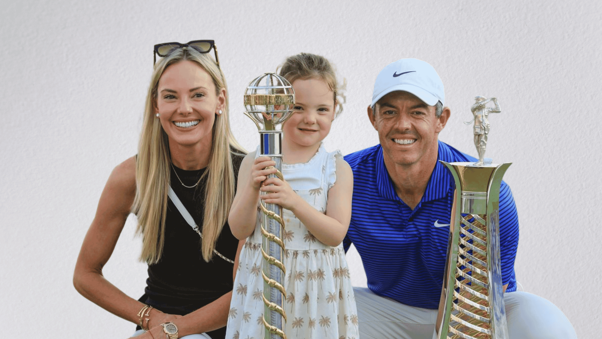 Rory McIlroy, Erica Stoll, and their young daughter smiling together with two trophies.