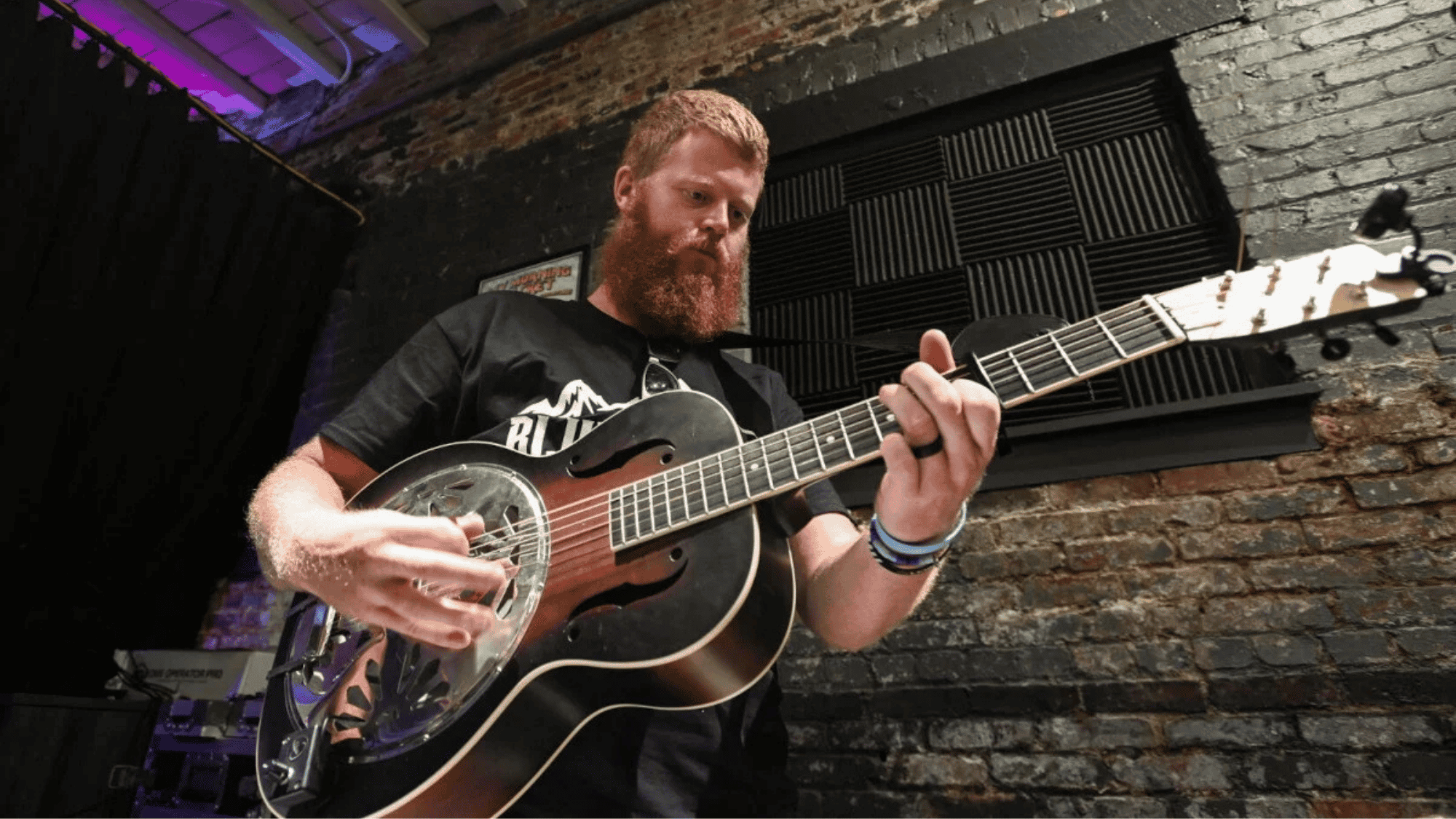 Country musician playing resonator guitar on a small indoor stage