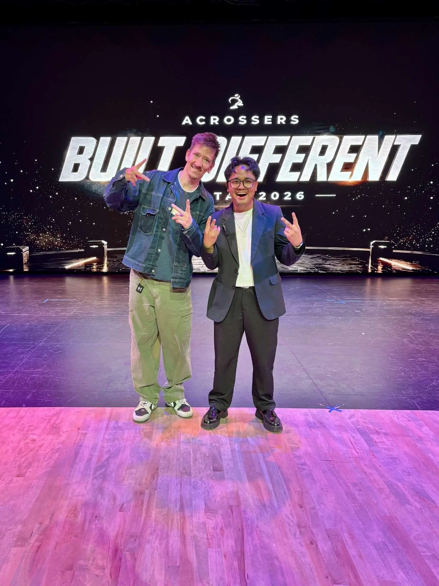 Two people posing on stage with "Built Different" sign in background