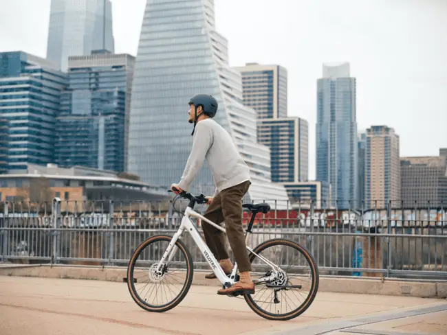 Man riding a bicycle on an urban waterfront path with city skyscrapers in the background