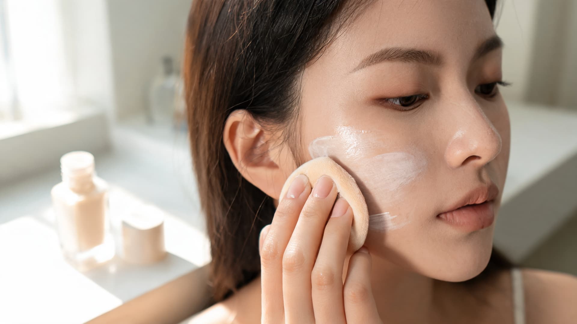 woman blending a lightweight base with a damp sponge for a soft natural finish