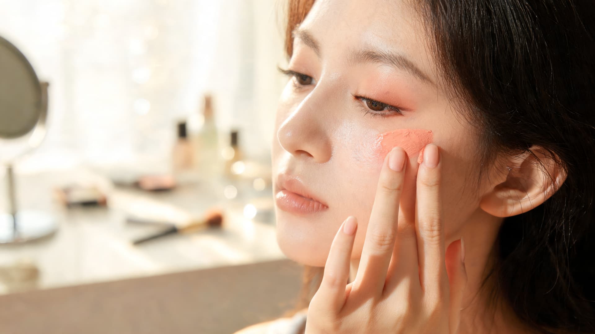 woman applying cream blush to the cheeks and blending it upward toward the temples