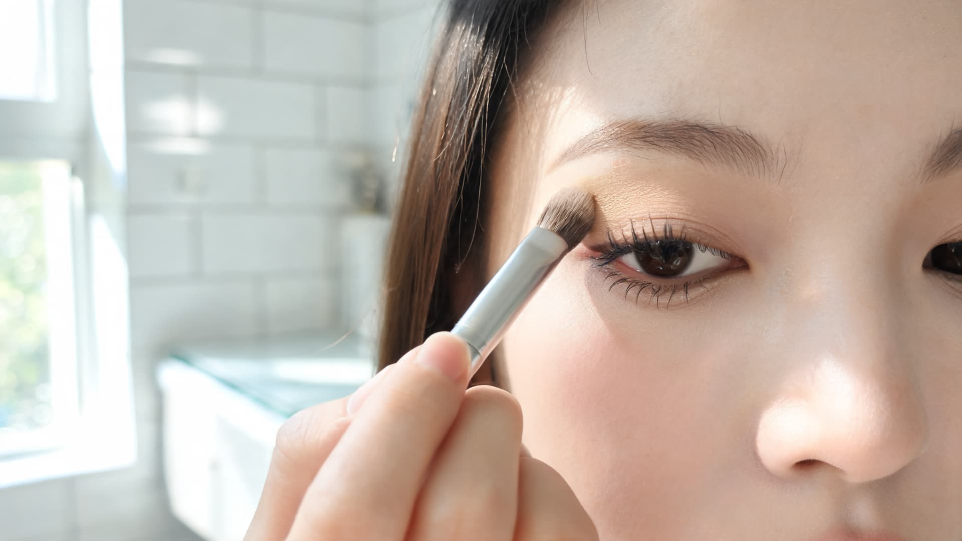 woman applying a neutral eyeshadow with softly defined lashes and natural eye makeup