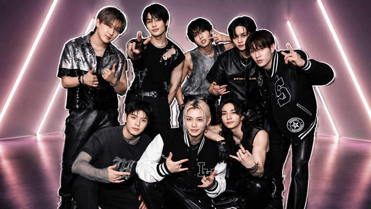 Stray Kids members posing in black outfits with a neon-lit backdrop