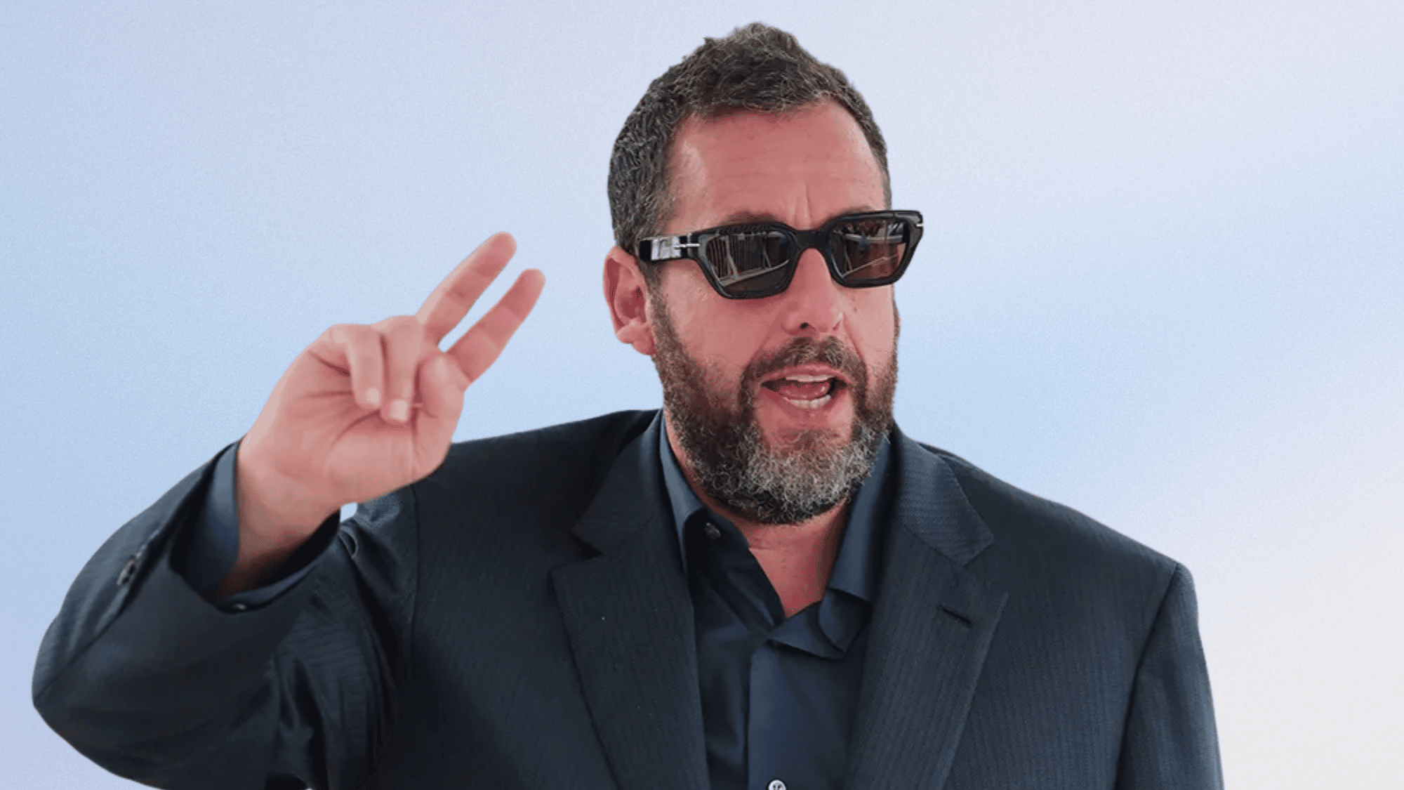 Man in dark suit and rectangular sunglasses flashing a peace sign outdoors