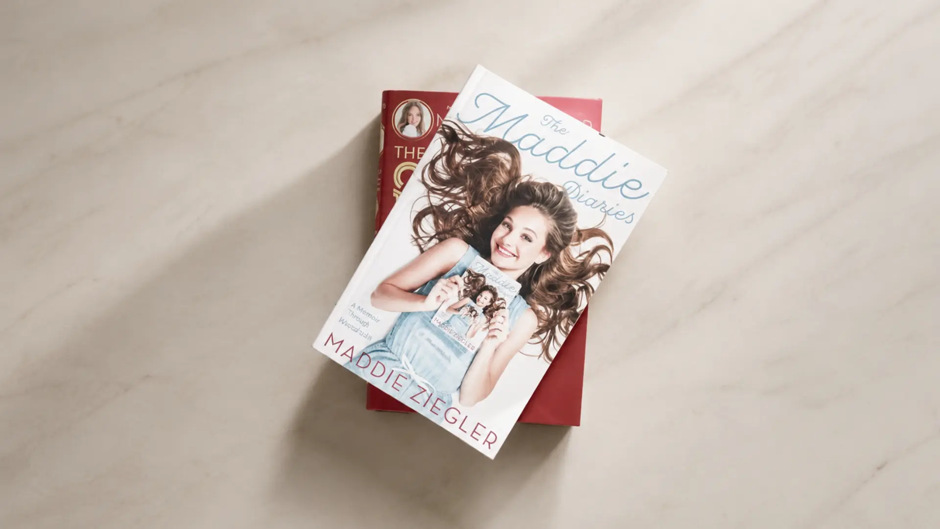 The Maddie Diaries book rests on a red book over a softly lit cream marble surface