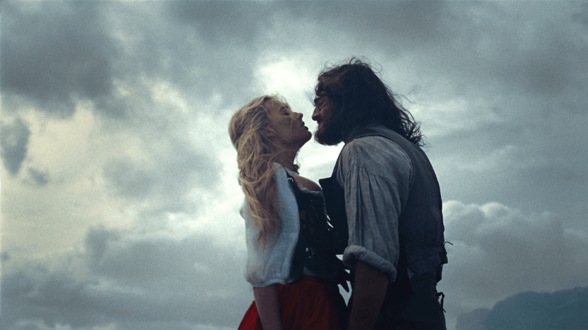 Couple leans close on stormy moors in a dramatic period romance scene