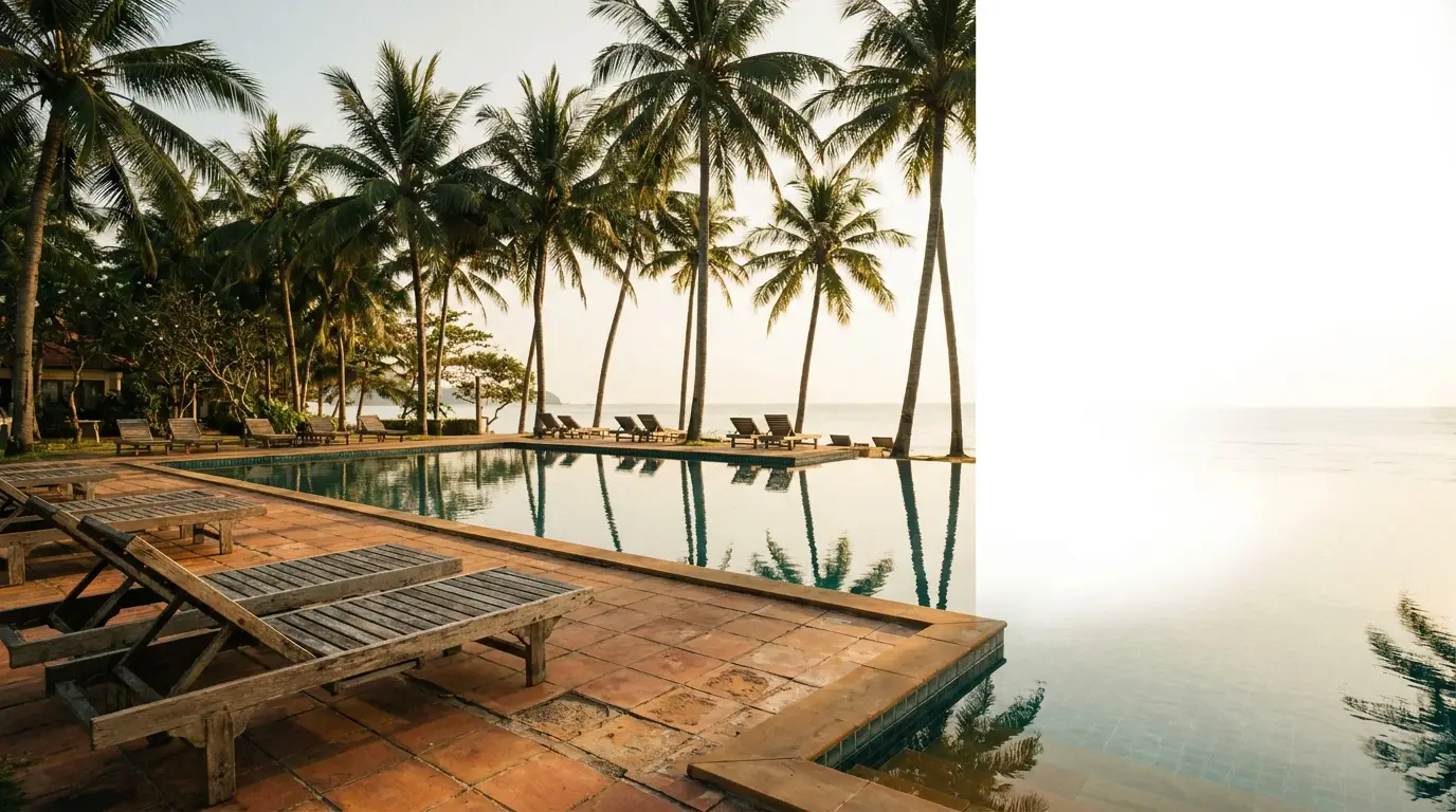 Poolside loungers and palm trees by the ocean at sunset