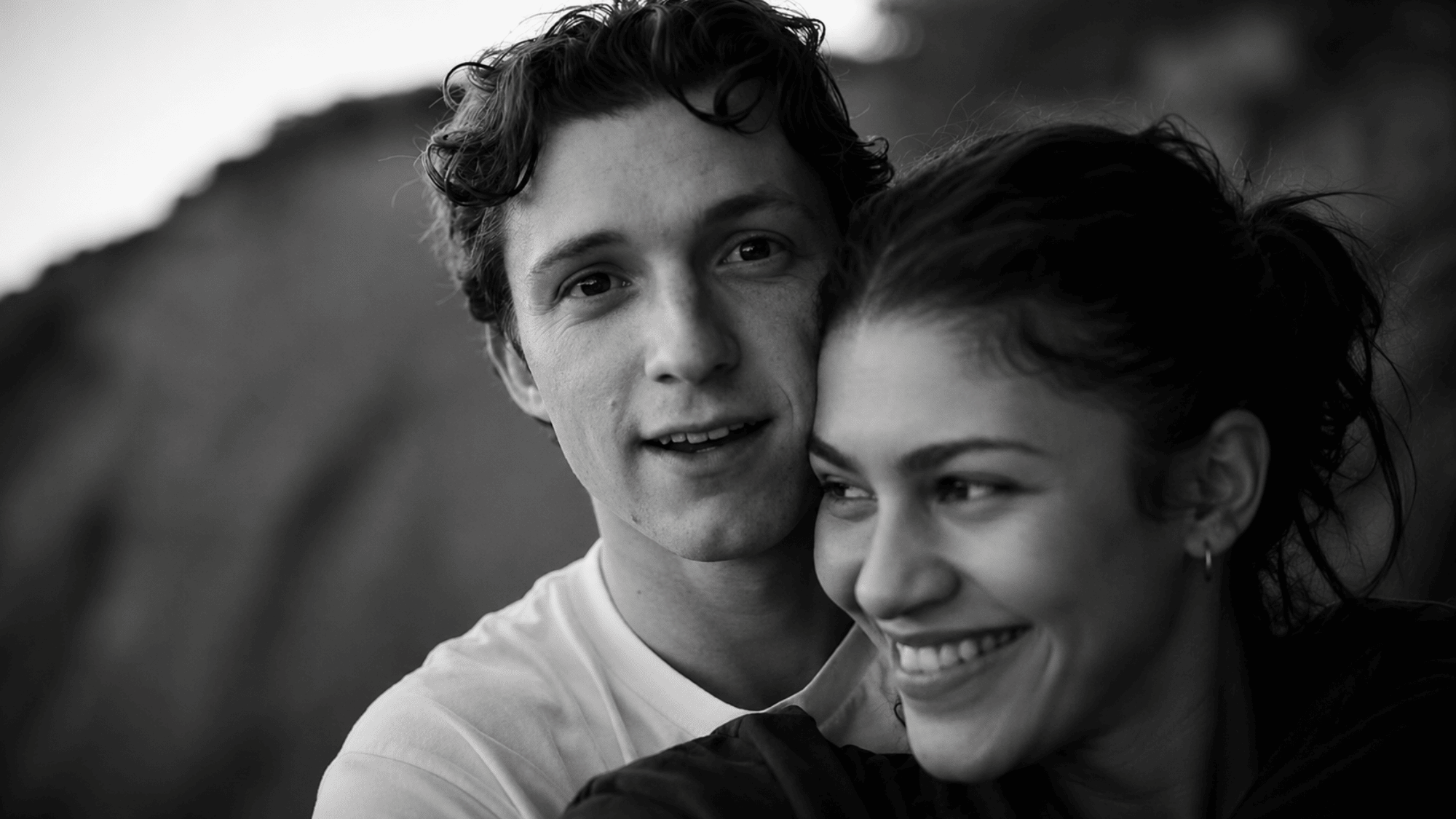 Black-and-white close-up of a smiling couple leaning together in a candid outdoor moment.