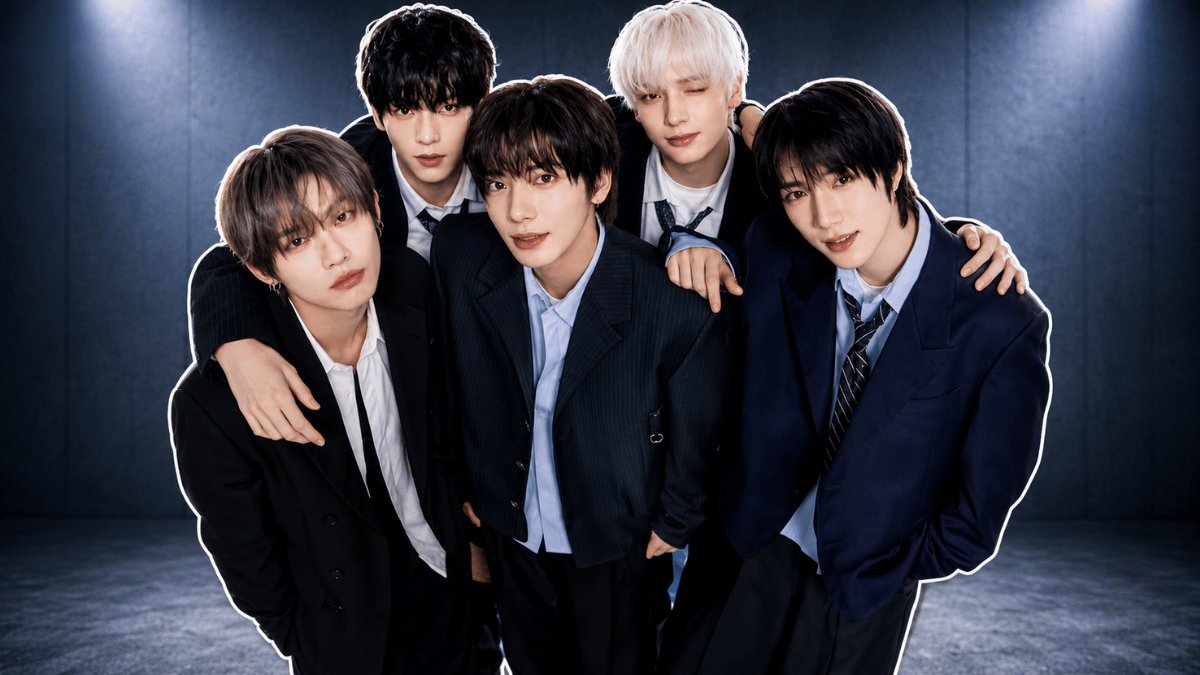 TXT members posing in formal suits at a dramatic studio backdrop