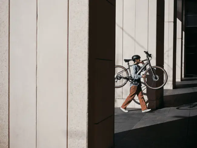 Person walking while carrying bicycle in urban area with tall beige columns