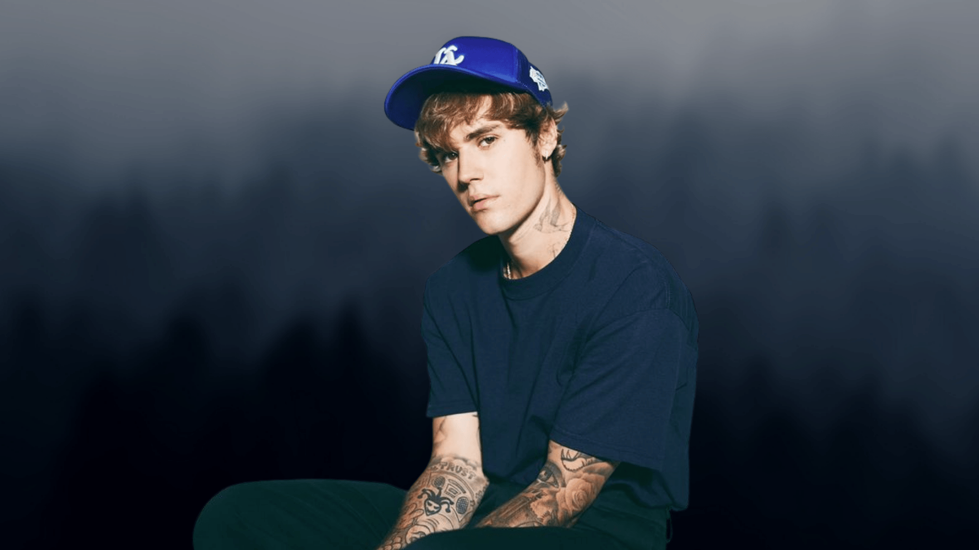 Justin Bieber wearing a blue cap and navy shirt against a dark background
