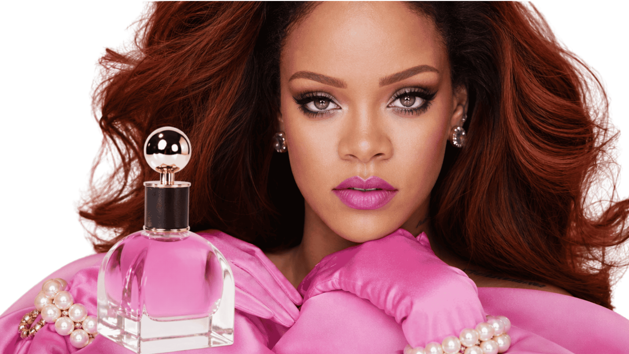Rihanna in pink satin and pearls posing beside a pink perfume bottle with gold cap
