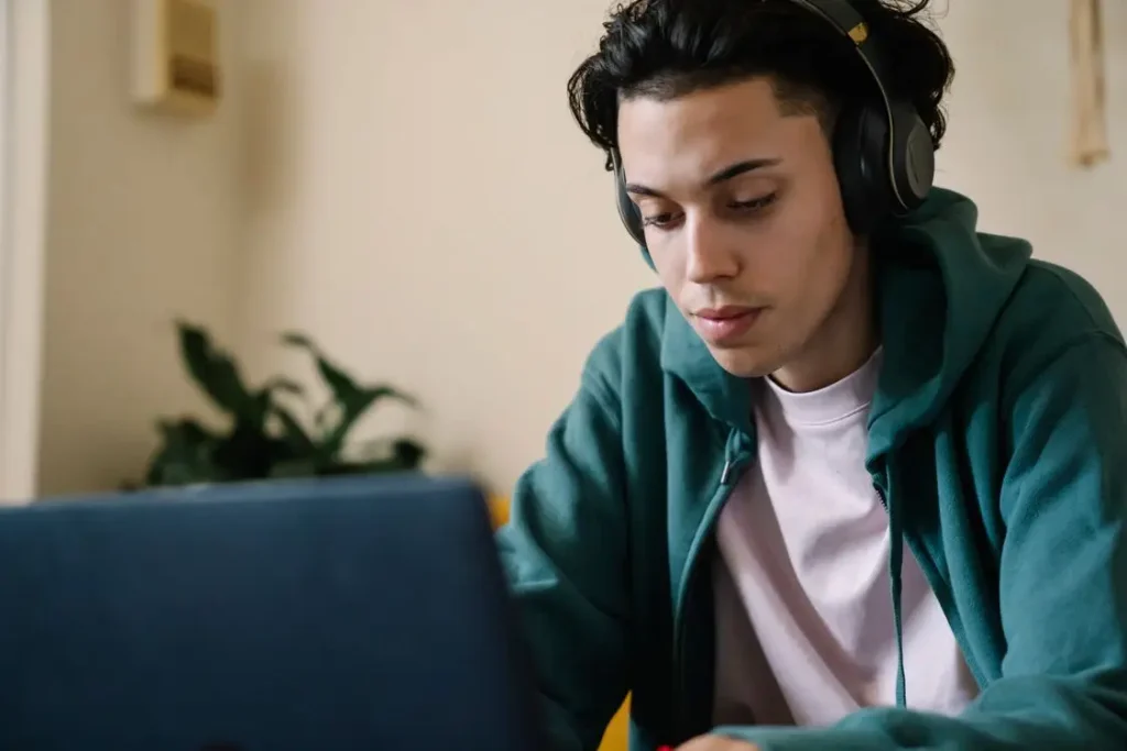 Person wearing headphones focused on laptop in softly lit room with a plant in background