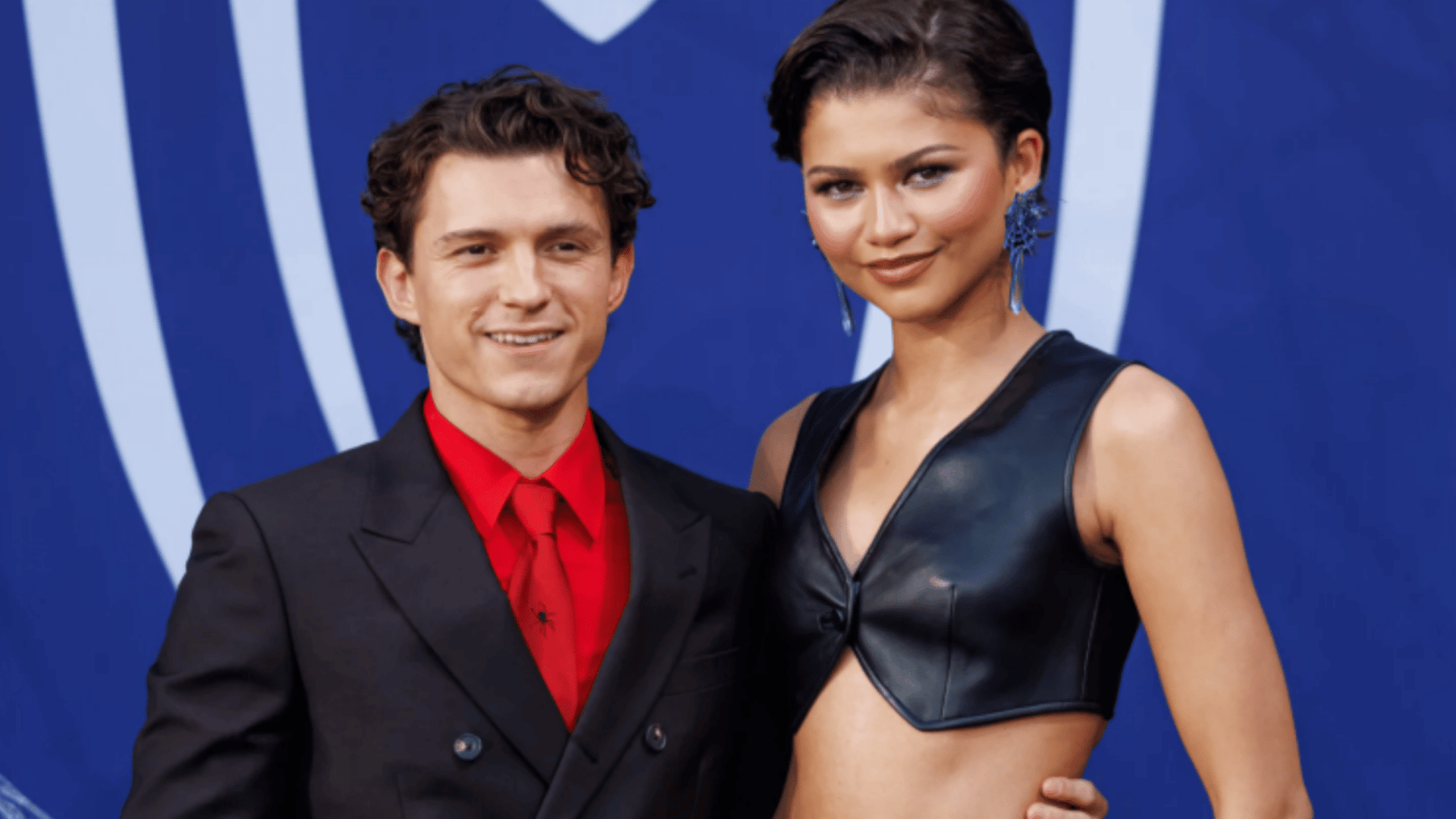 Tom Holland and Zendaya posing together at a red carpet event in stylish formal outfits.