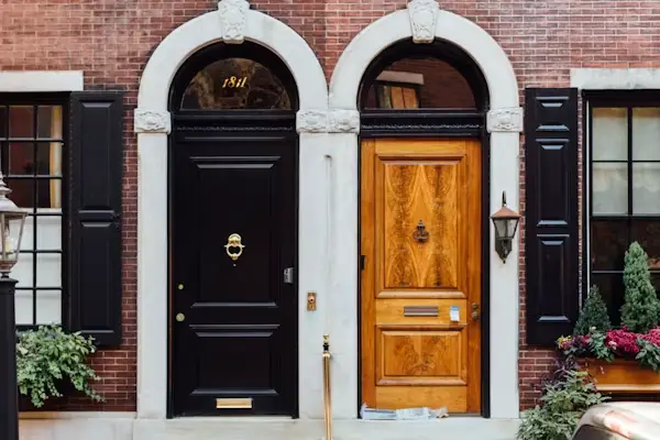 Adjacent black and wooden doors with arched frames on red brick townhouse facade