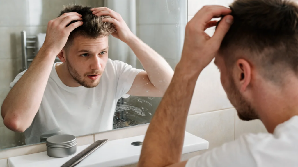 young man checking and styling his short hair in a bathroom mirror beside a comb and hair product