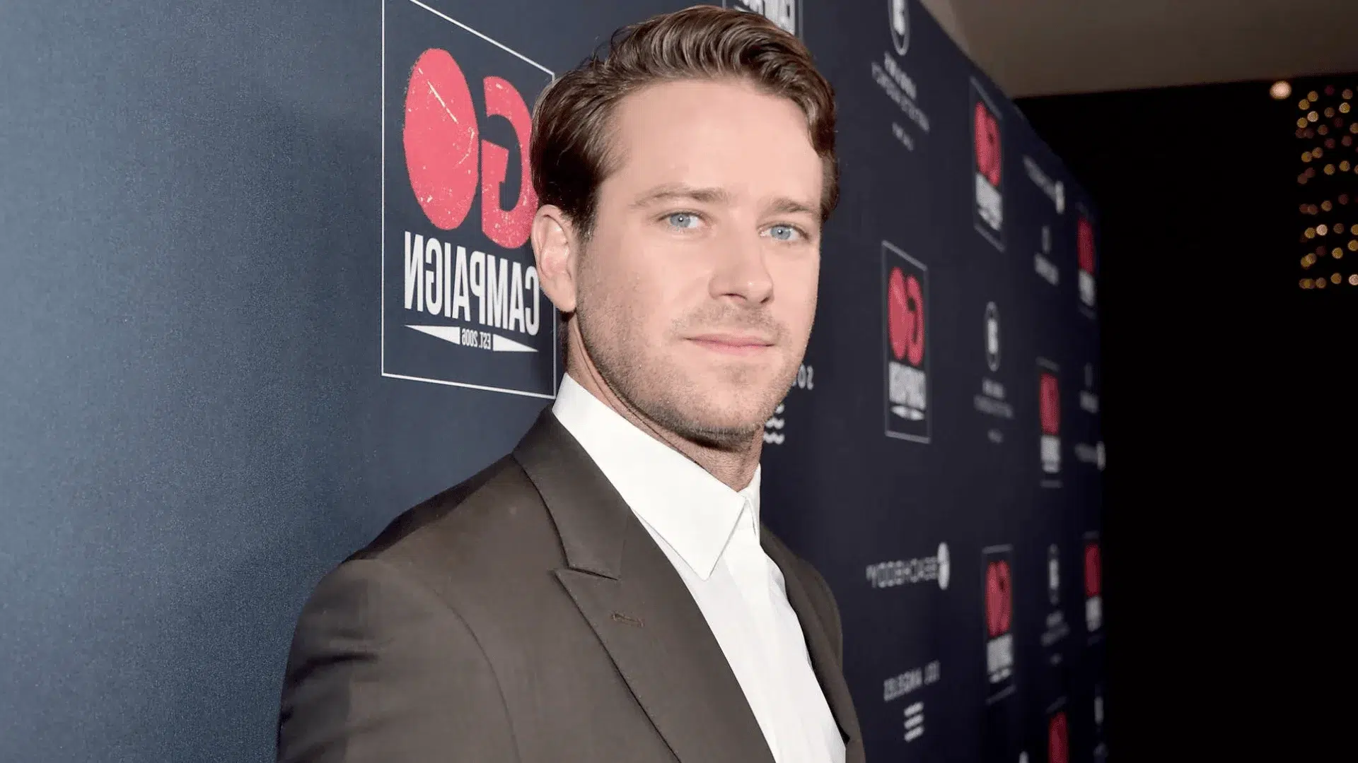 armie hammer wearing a brown suit posing at the go campaign event step and repeat