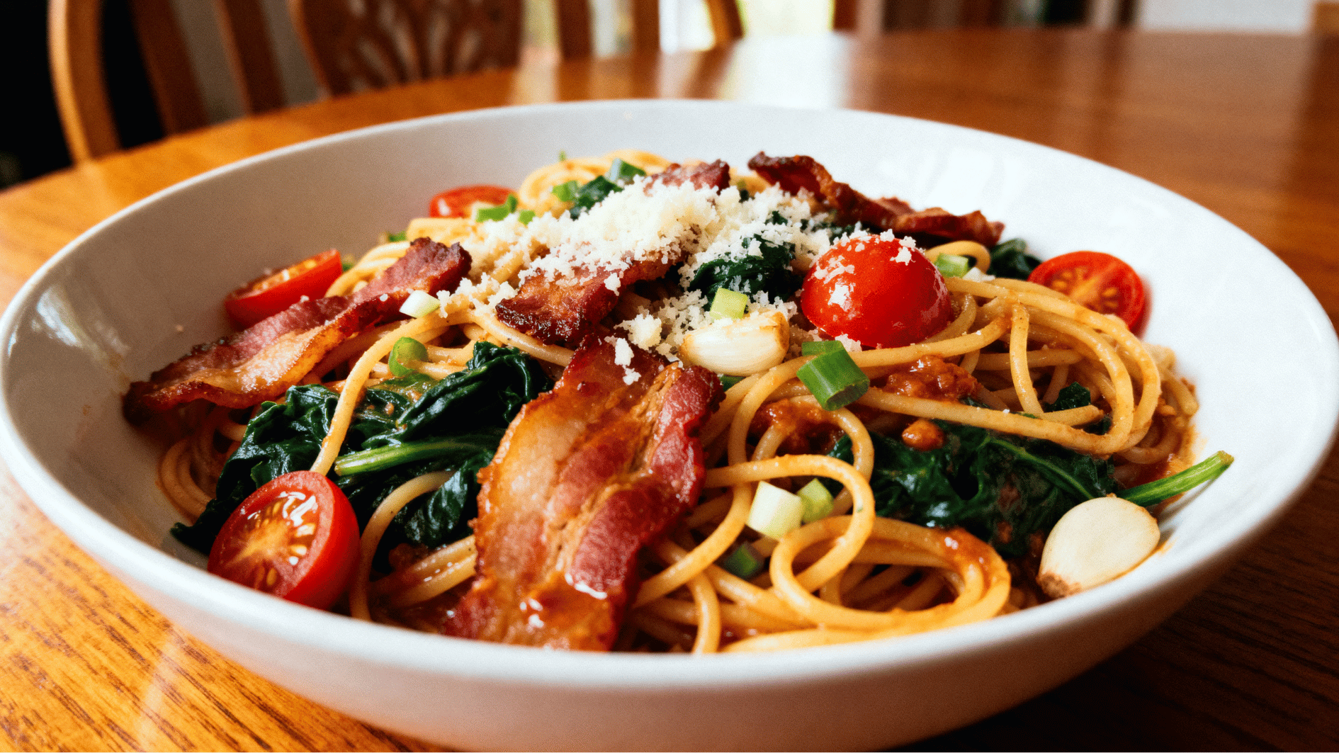 bacon vegetable pasta with crispy bacon, noodles, spinach, tomatoes, and parmesan served in a bowl meal