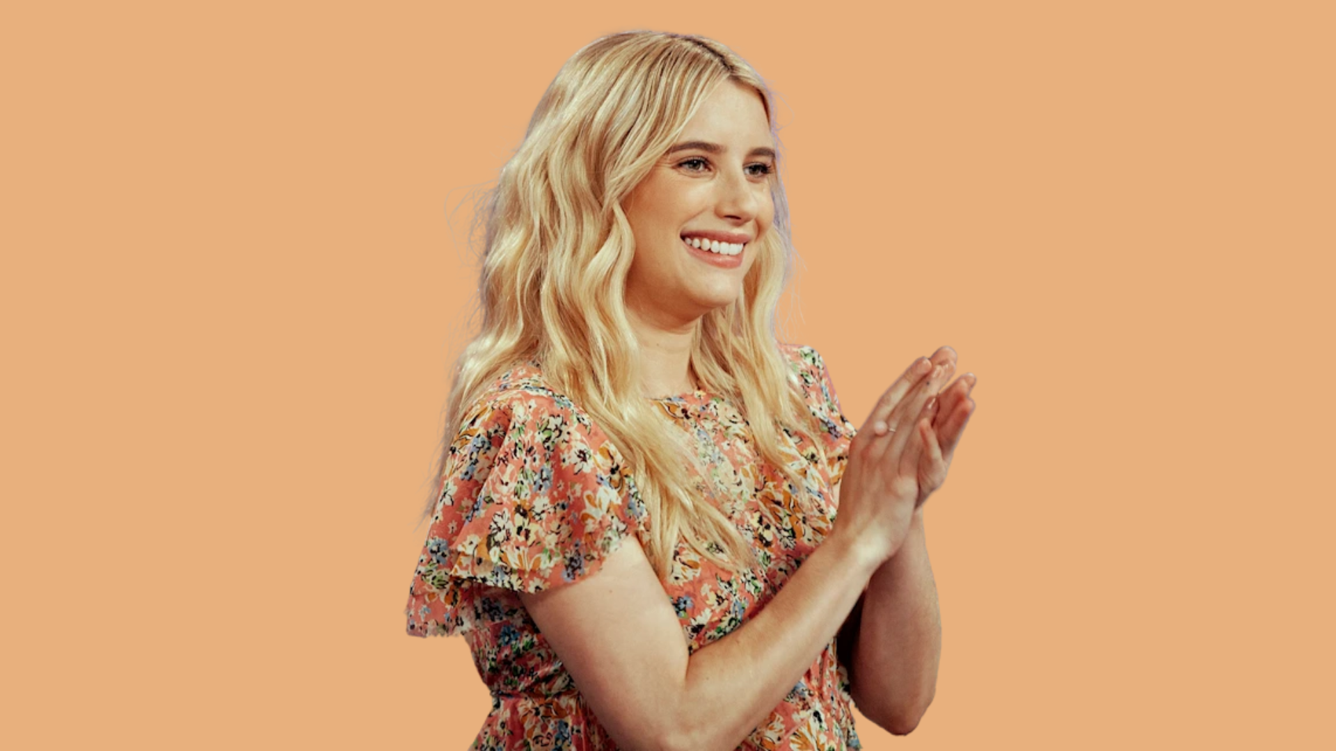 blonde woman in floral dress smiling and clapping against an orange background