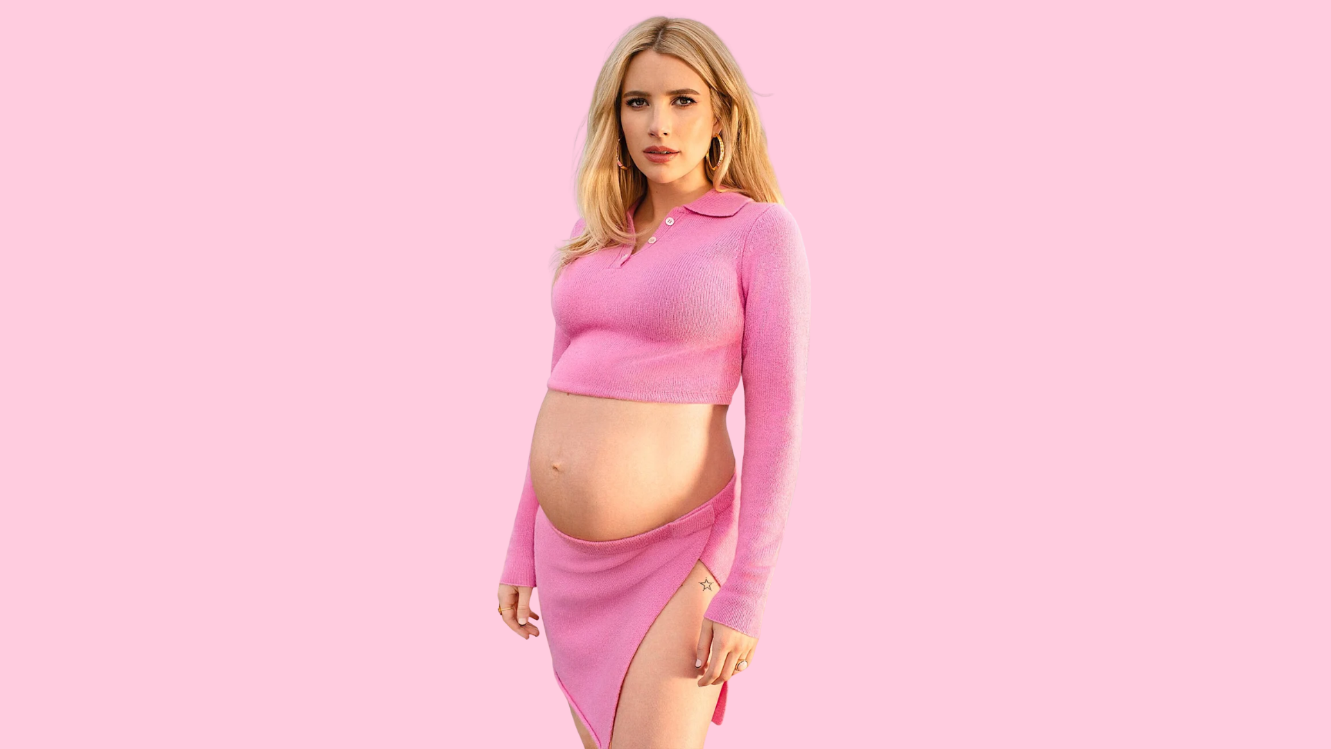 blonde woman showing baby bump in pink cropped top and skirt against pink background