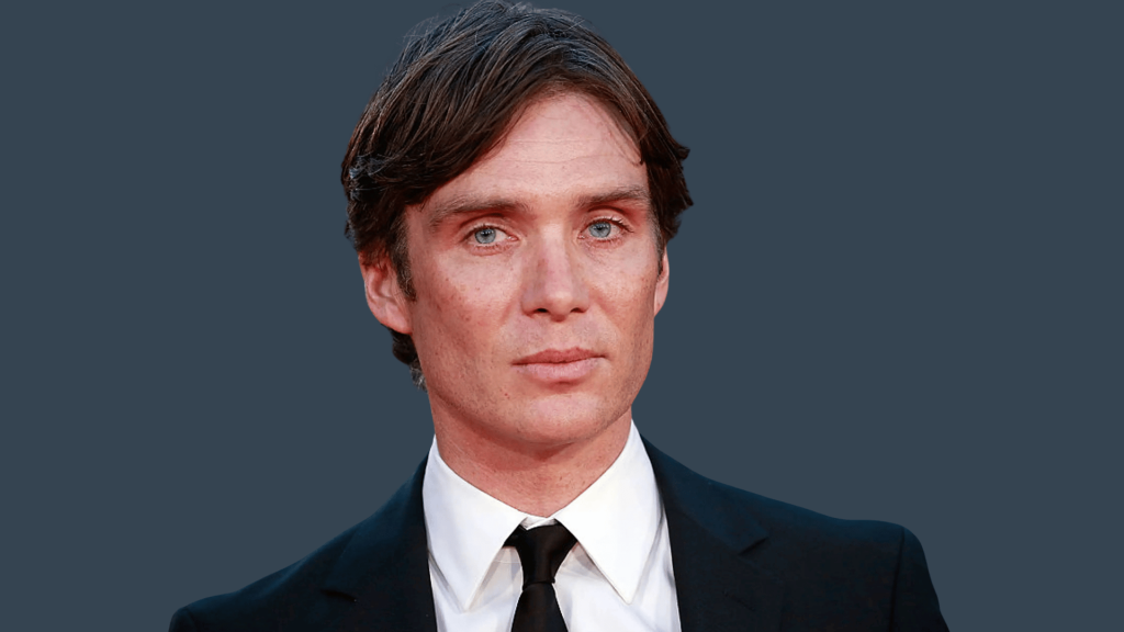 cillian murphy in a black suit and tie against a plain dark gray background wall