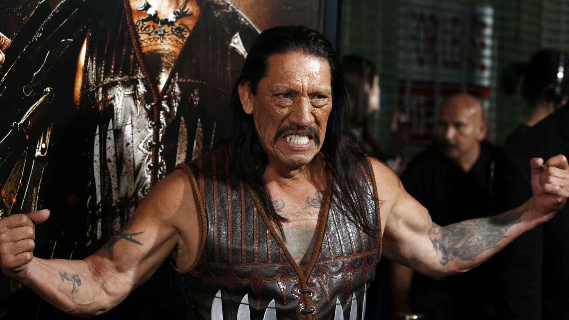 Close-up vintage portrait of a Danny trejo with dark hair and a mustache smiling slightly while facing the camera