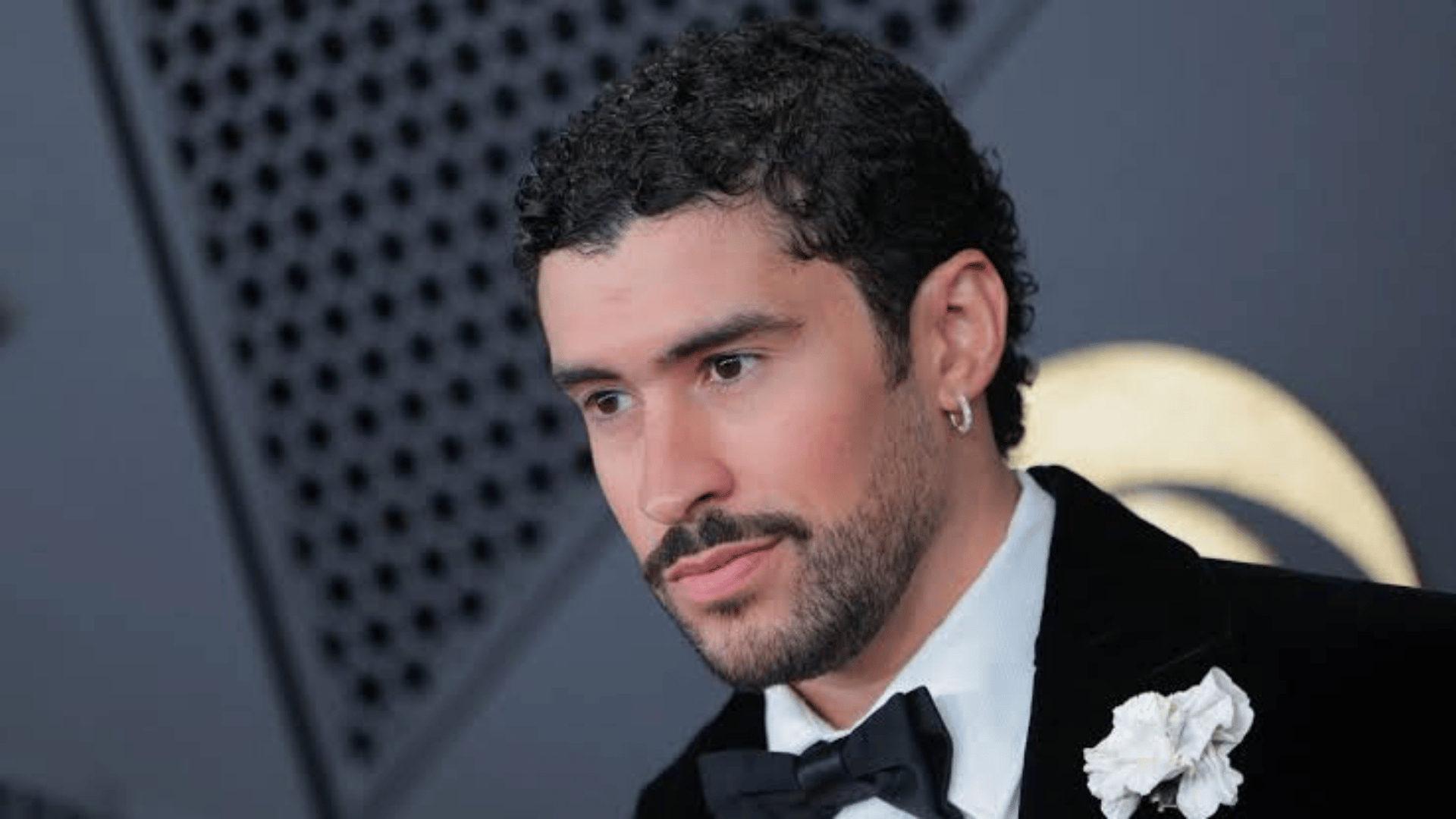 Bad Bunny wearing a black tuxedo and white flower while posing at a formal event